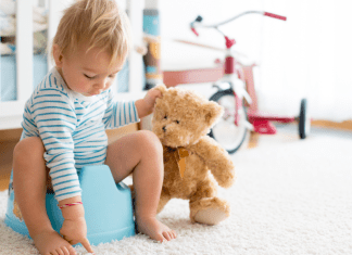 A boy sitting on a potty holding his teddy bear.