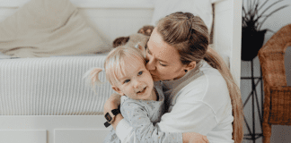 A mother hugging and kissing her daughter.