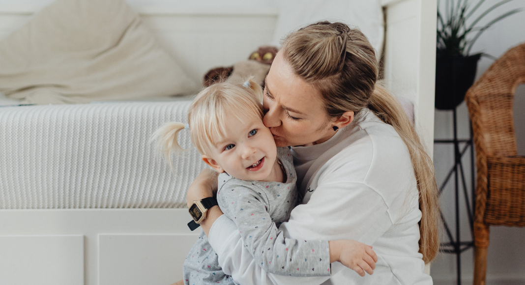 A mother hugging and kissing her daughter.