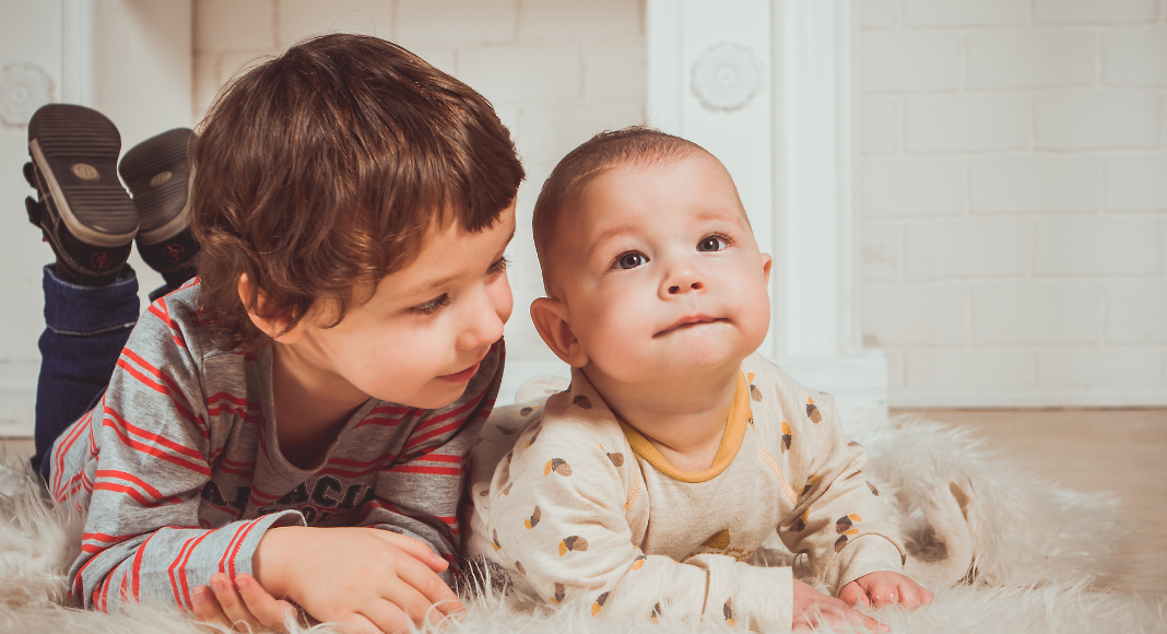A toddler and baby laying on their bellies.