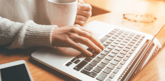 My Saved Posts A woman typing on the computer holding a coffee cup.