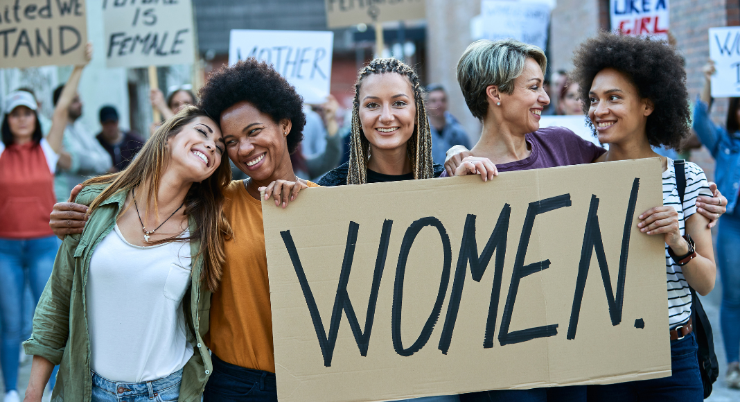 Women holding a sign that says "Women"