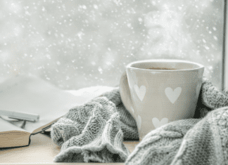 A mug of coffee wrapped in a scarf by a winter window.