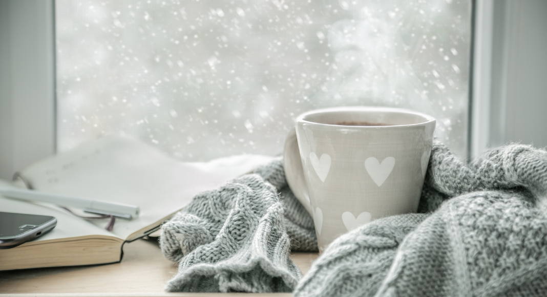A mug of coffee wrapped in a scarf by a winter window.