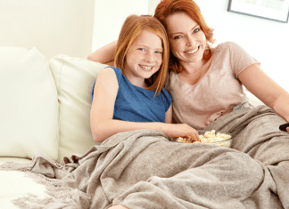 A mother and daughter under a blanket watching a movie.