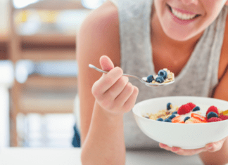 A woman eating a bowl of cereal with fruit.