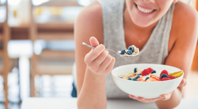 A woman eating a bowl of cereal with fruit.