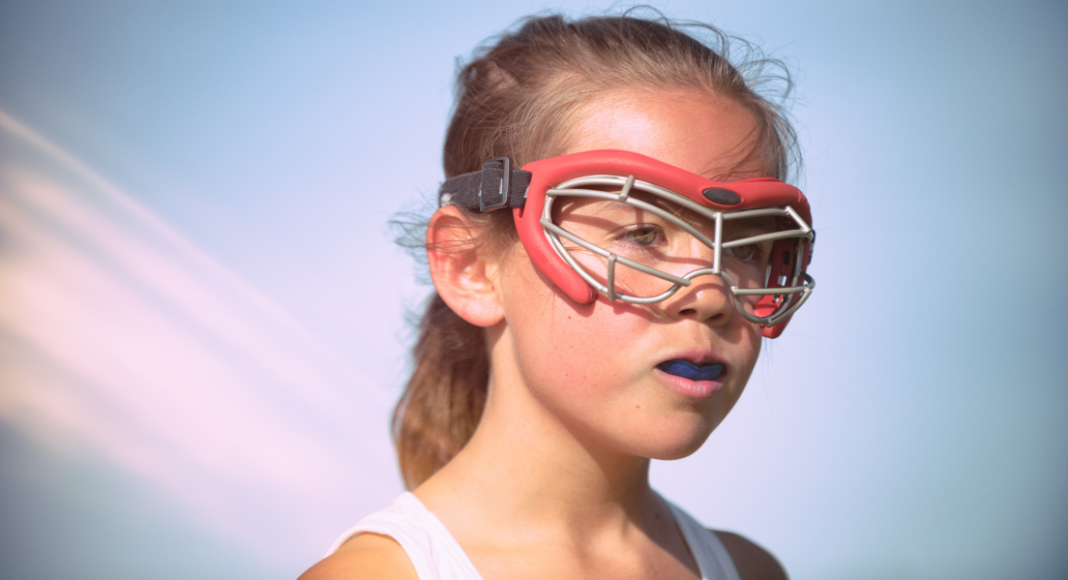 A young girl lacrosse player wearing googles.