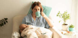 A mom in her fourth trimester holding a baby and drinking coffee.