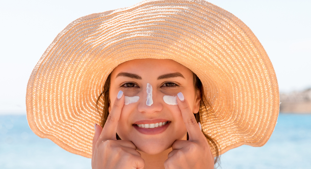 A woman applying sunscreen to her face.