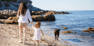 A mom walking on the beach with her daughter and dog.
