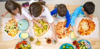 Kids putting toppings on their pizzas.