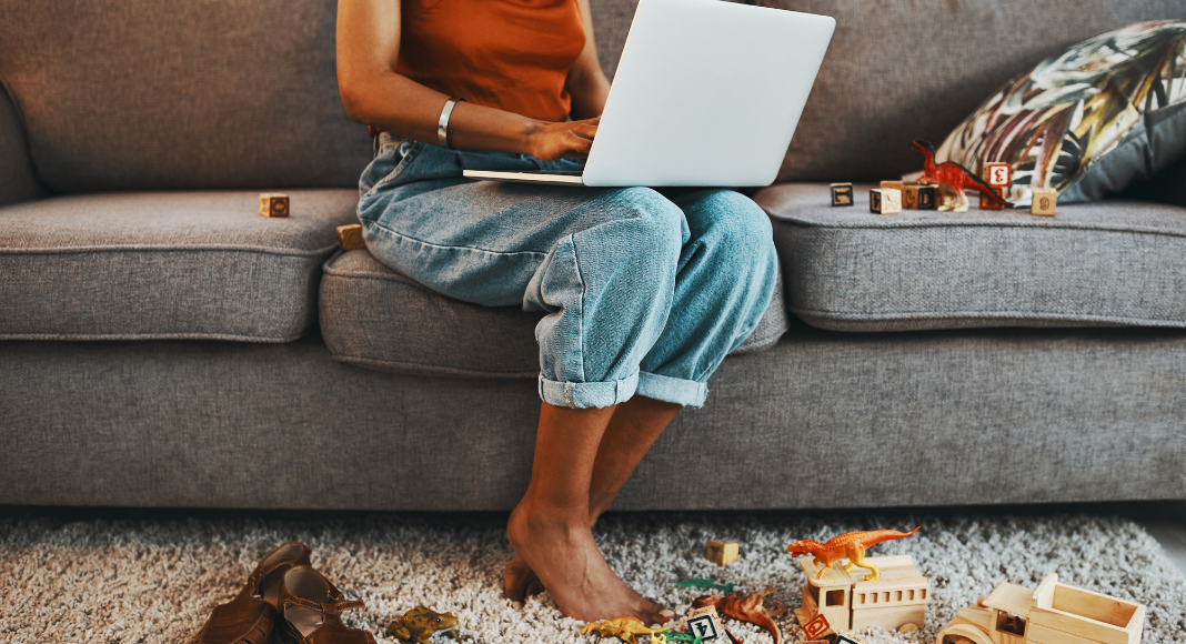 A woman trying to work on a computer surrounded by a mess of toys.