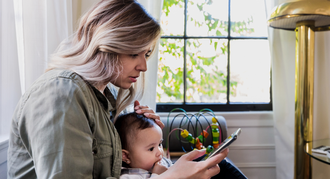A new mom checking social media while holding her baby.