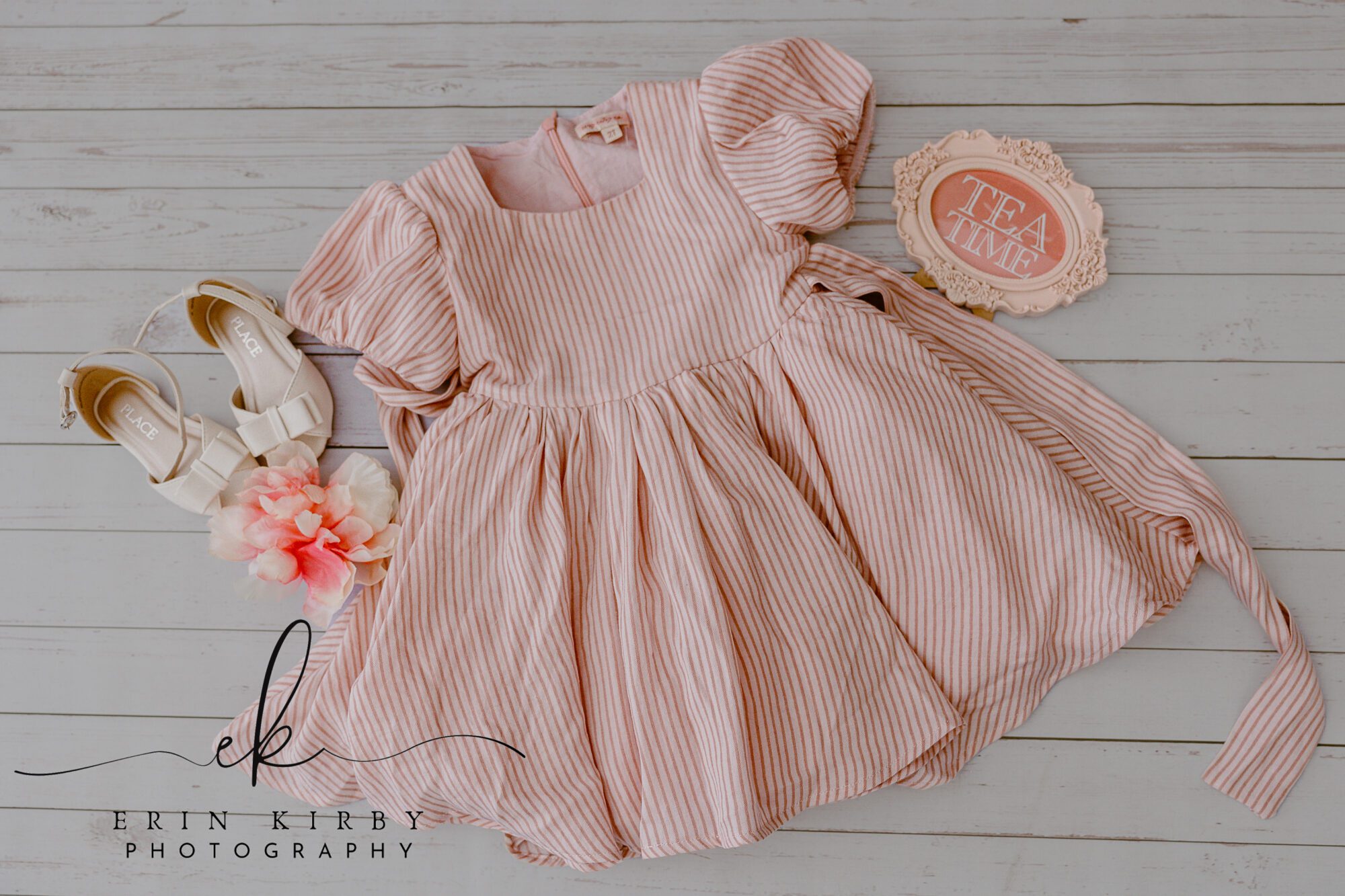 A pink dress is shown with white dress shoes, a "tea time" picture in frame, and pink flowers. The floor is white wood.