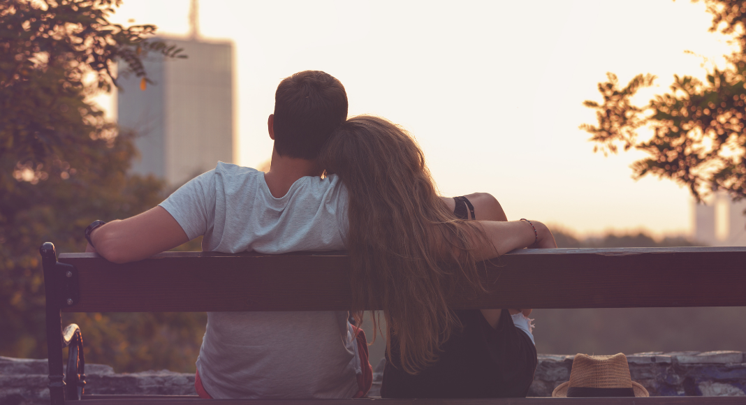 A couple cuddling together on a park bench.