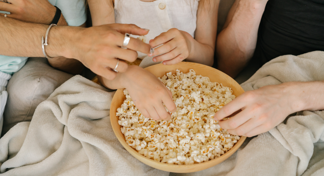 Hands reaching for a bowl of popcorn.