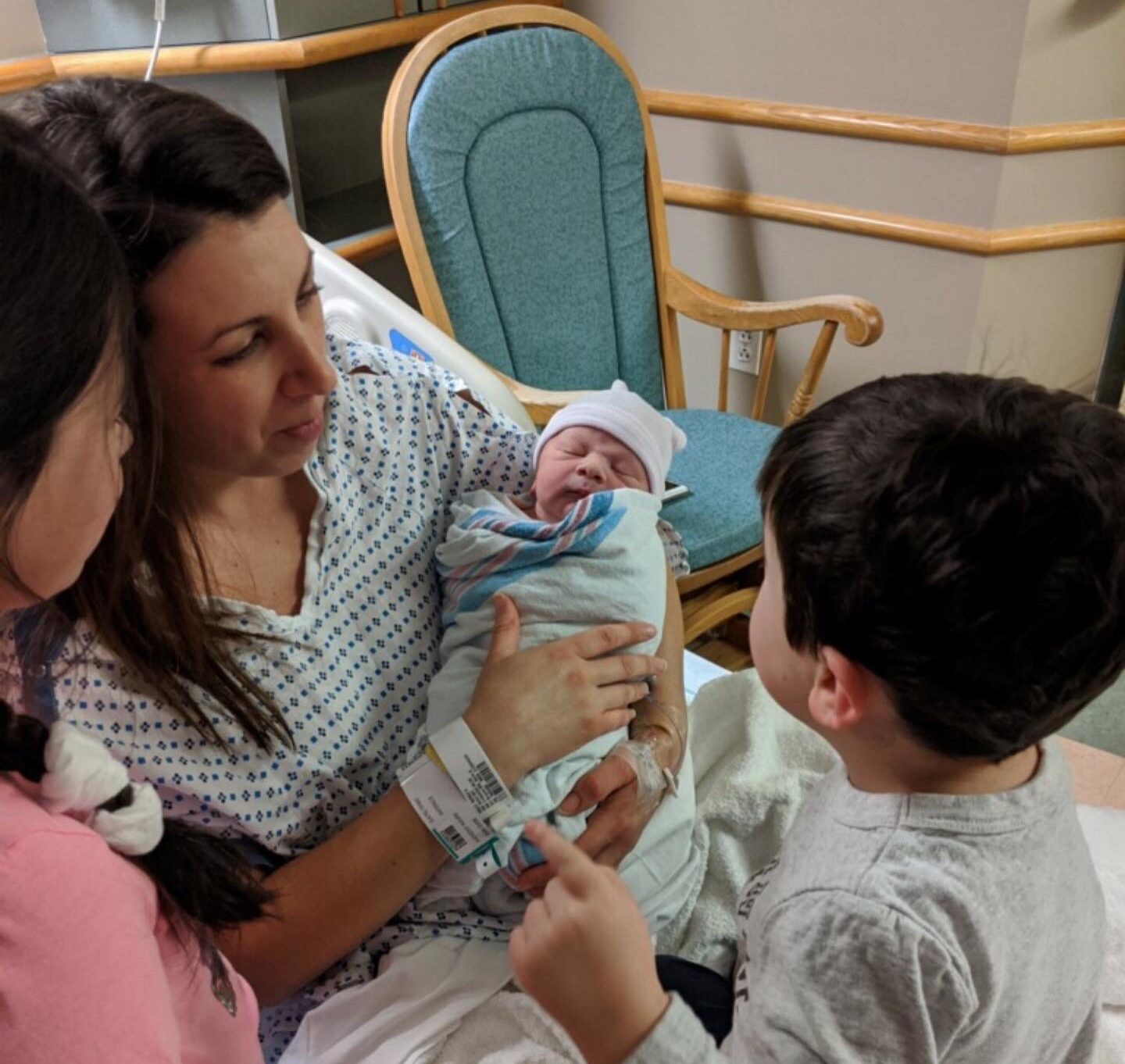 A mother holding her baby so the siblings can see. 