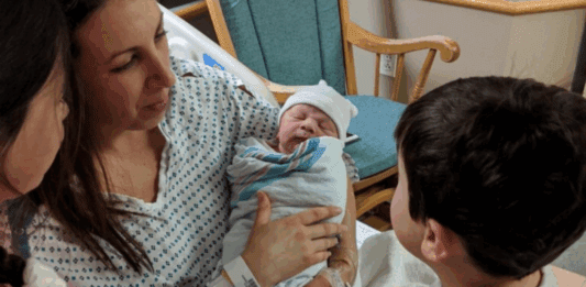 A mom holding a newborn for her children to see.