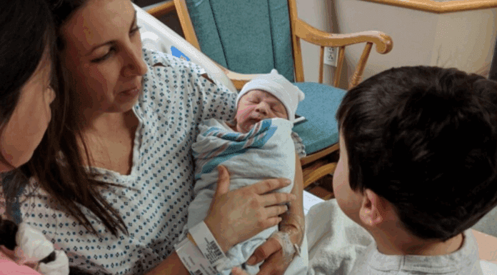 A mom holding a newborn for her children to see.