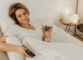 A woman holding a tv remote and glass of wine.