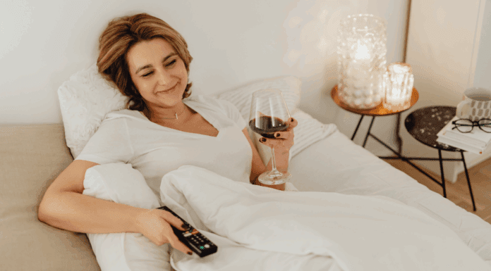 A woman holding a tv remote and glass of wine.
