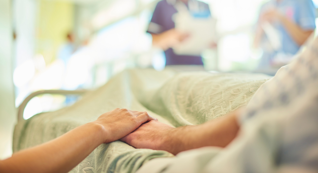 People holding hands in a hospital bed.