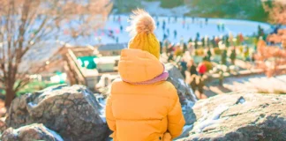 Child in orange coat and hat overlooking the ice rink during Thanksgiving Weekend in NYC