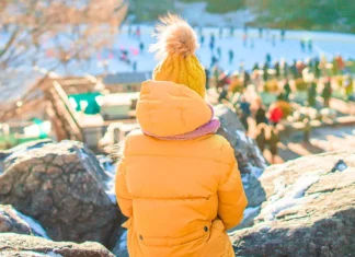 Child in orange coat and hat overlooking the ice rink during Thanksgiving Weekend in NYC
