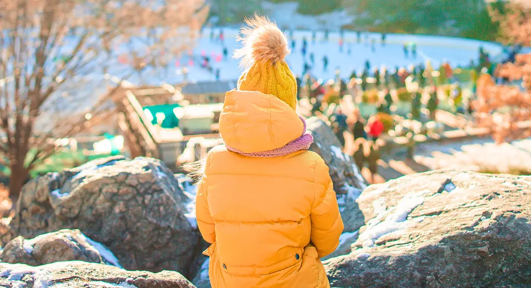 Child in orange coat and hat overlooking the ice rink during Thanksgiving Weekend in NYC