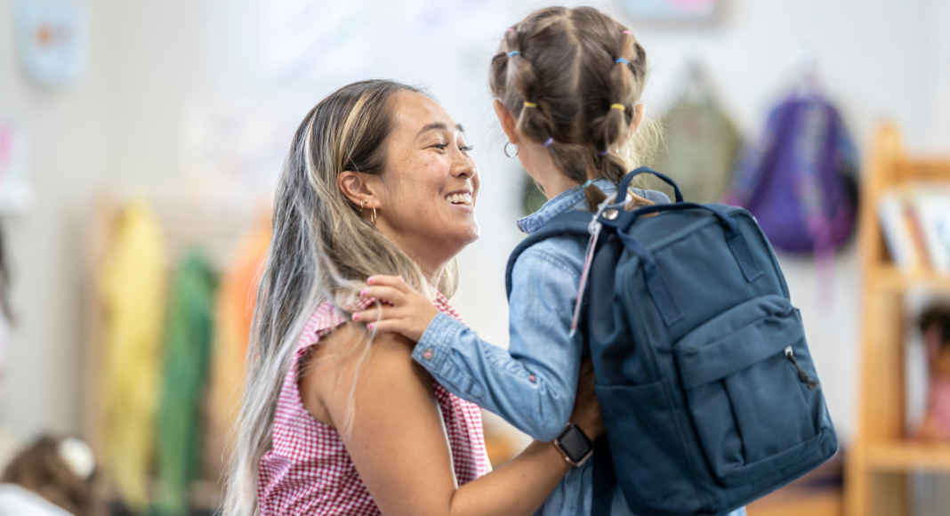 A mom saying goodbye to her daughter at school drop-off.