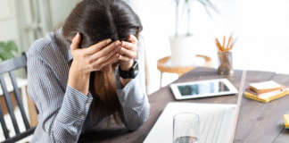 The Pressure You Don’t See A woman holding her head in front of her computer.
