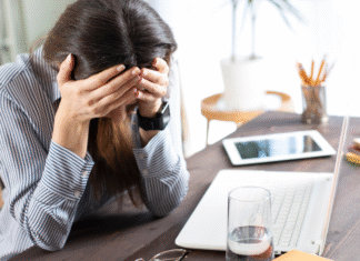 The Pressure You Don’t See A woman holding her head in front of her computer.