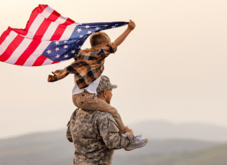 A veteran holding his son on his shoulders as the boy holds the American flag.