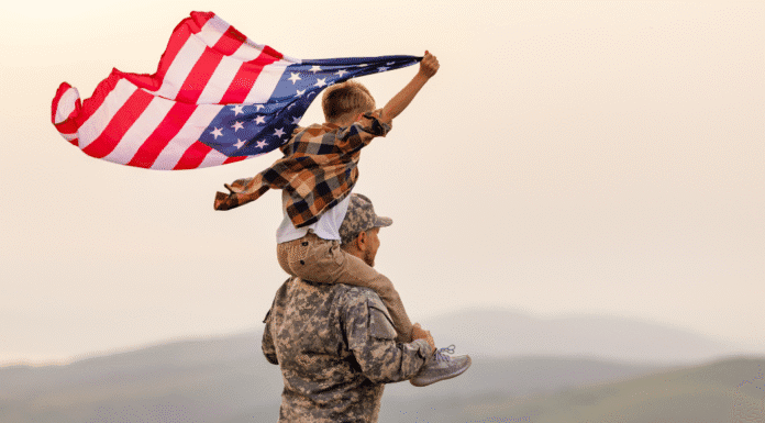 A veteran holding his son on his shoulders as the boy holds the American flag.