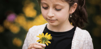 Ways to Teach Kids About Gratitude this Thanksgiving and Beyond A girl looking at a flower.