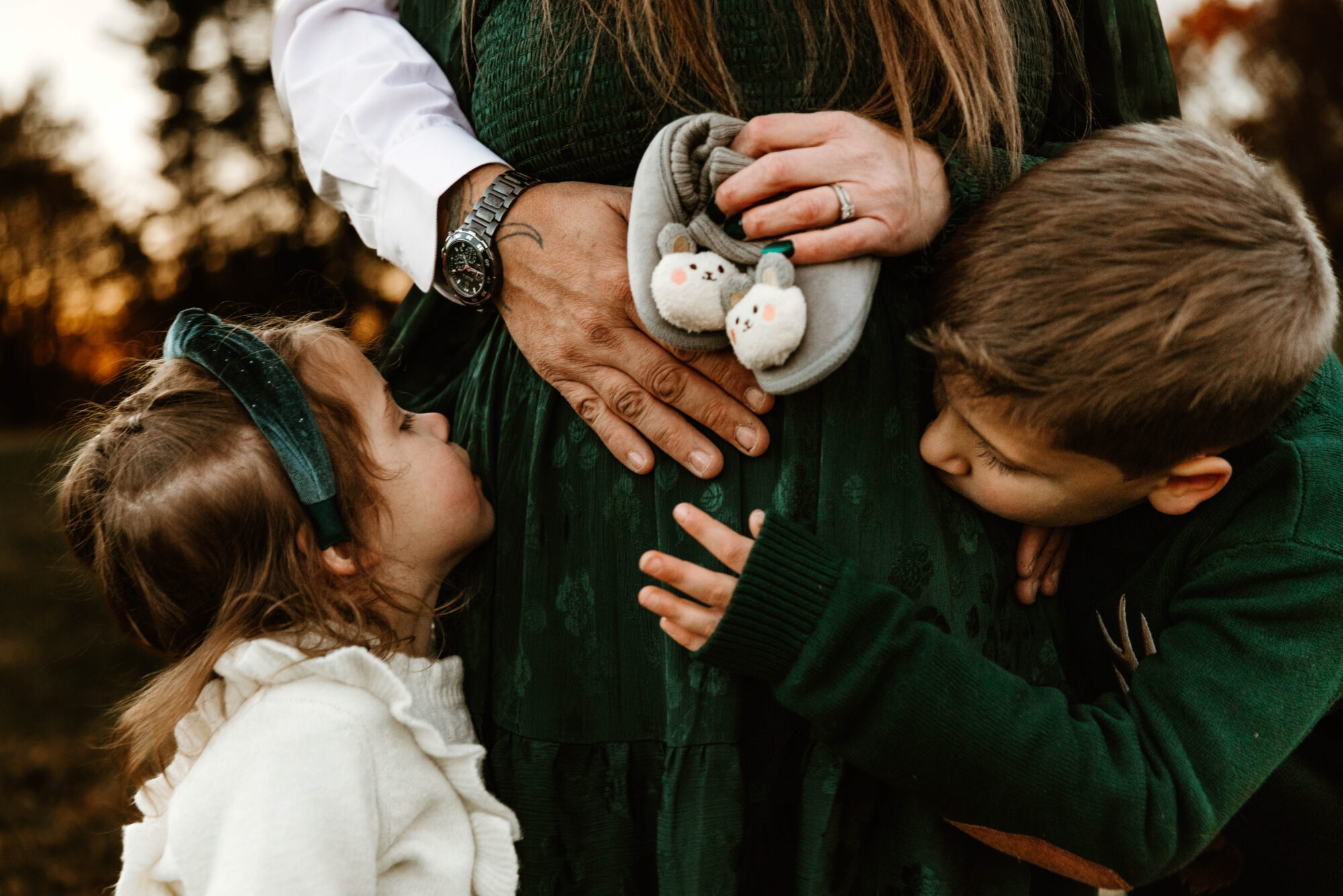 A family of 4 holds a mother's pregnant belly. 