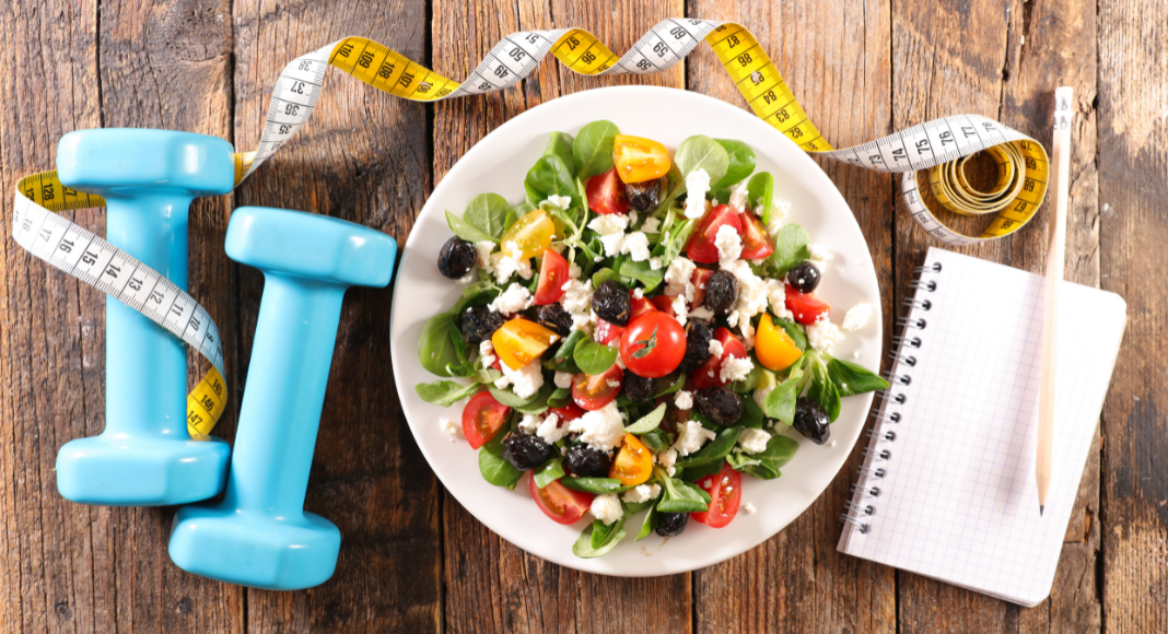 fitness, health, and wellness A healthy salad next to 5lb weights and a notebook.
