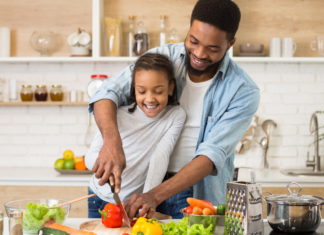 A dad and daughter chopping vegetables in the kitchen.
