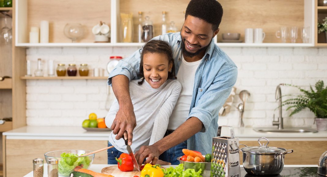 A dad and daughter chopping vegetables in the kitchen.