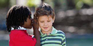 Helping Kids Navigate Friendships With Kindness and Confidence A boy whispering in a friend's ear.