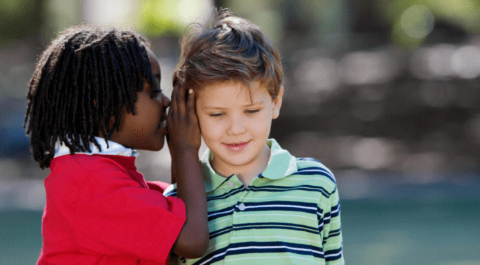 Helping Kids Navigate Friendships With Kindness and Confidence A boy whispering in a friend's ear.
