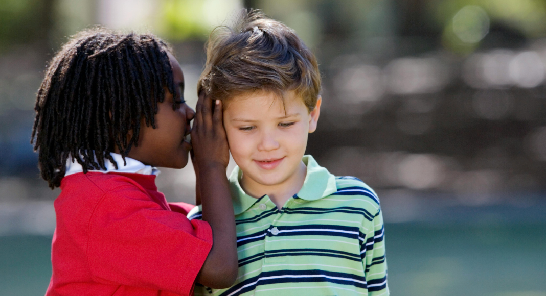 A boy whispering in a friend's ear. 