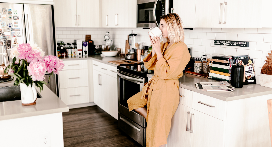 A woman drinking her first cup of morning coffee in the kitchen. 