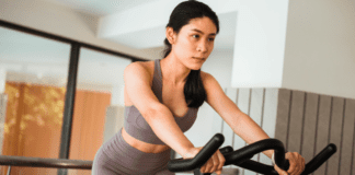 Why Working Out Feels So Hard as a Mom (And It’s Not Your Fault) A woman on a stationary bike.