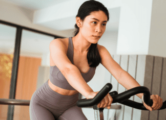 Why Working Out Feels So Hard as a Mom (And It’s Not Your Fault) A woman on a stationary bike.
