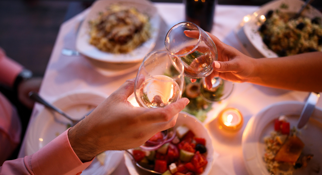 date night guide Wine glasses being held over a table full of food.