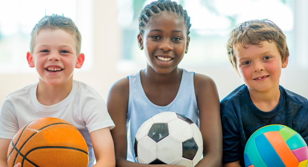 Kids holding sports balls for summer camp.
