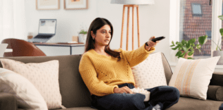 A woman on the couch with a TV remote and popcorn.