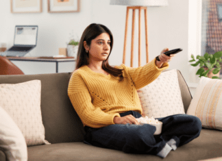 A woman on the couch with a TV remote and popcorn.